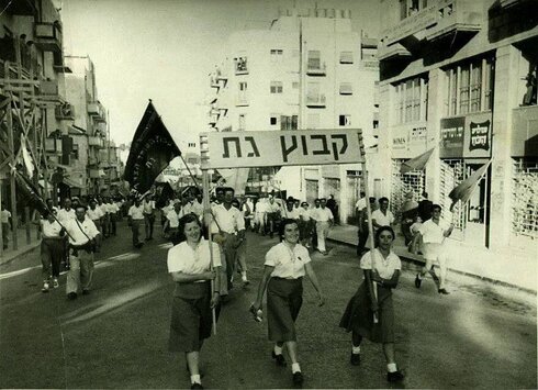 שלוש נשים נושאות את שלט קיבוץ גת בהפגנת האחד במאי בתל אביב בשנת 1955.מימין- זיווה פרץ ומשמאל שרה גנדלמן. 